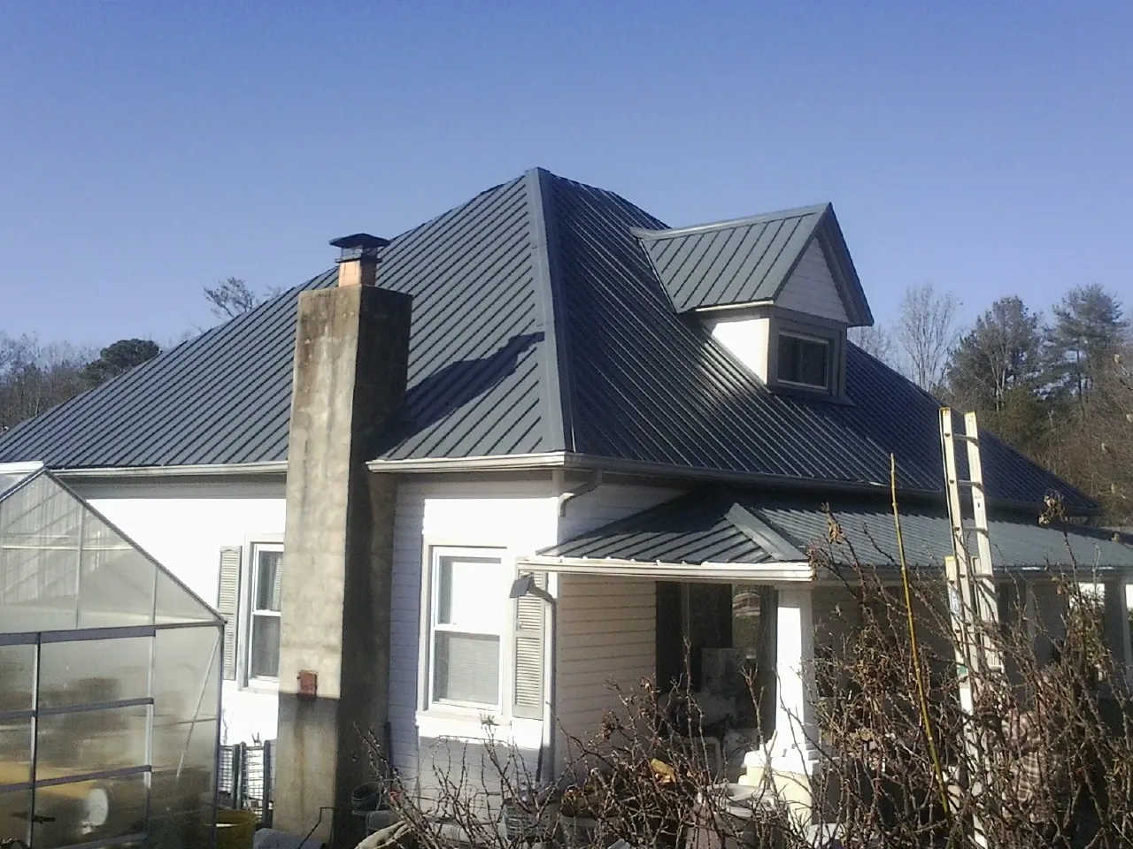 Dark blue standing seam metal roof on a white farmhouse with dormer — Slate & Tile Roof Repair by Roofing Brothers in Vancleave