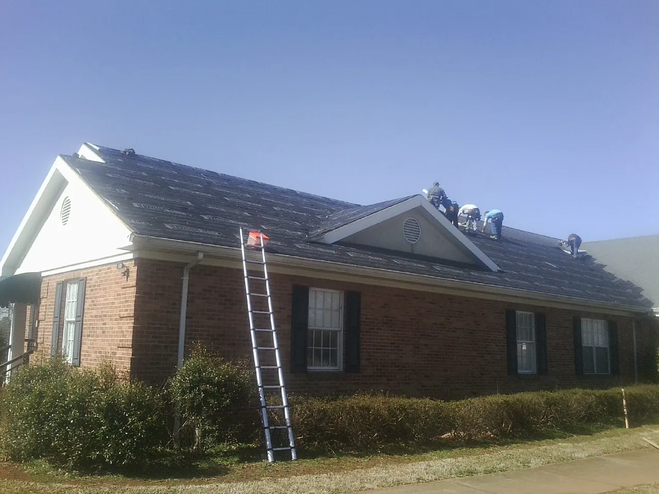Crew tearing shingles off a brick ranch roof with a ladder set — Emergency Roof Repair work by our crew in Vancleave