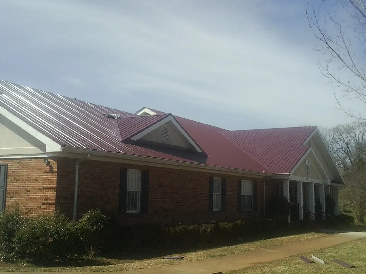 Red metal roof with gabled entries on a long brick building, from a Hail Damage Roof Repair job in Vancleave