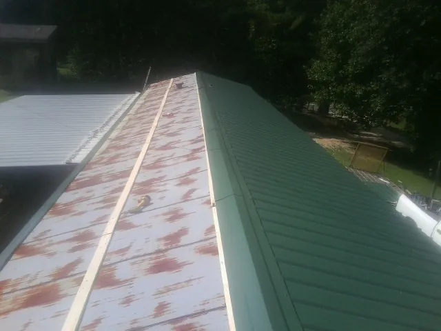Old rusted panels beside newly installed green metal roofing — Wind Damage Roof Repair by Roofing Brothers in Vancleave