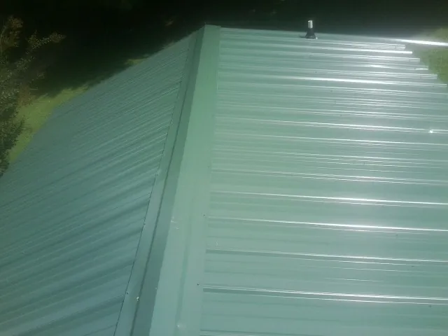 New green metal panels meeting at the ridge of a roof — Flat Roof Repair work by our crew in Vancleave