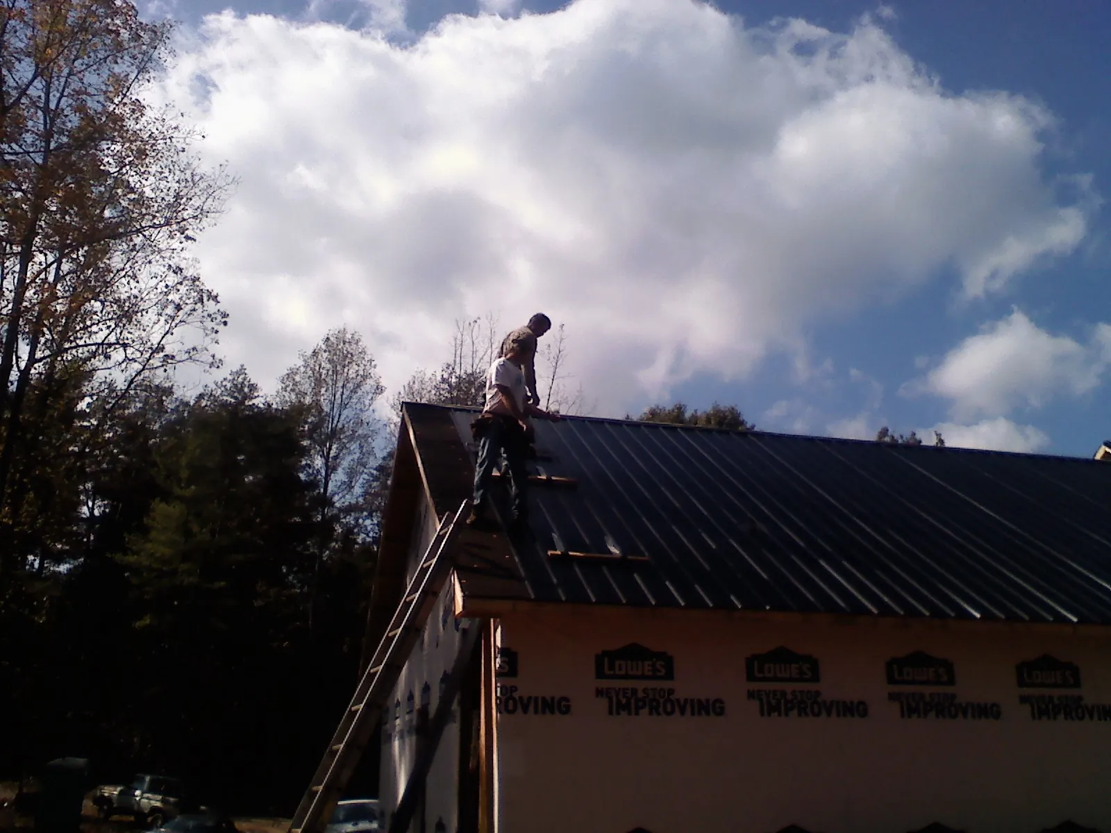 Roofer fastening dark metal panels high against a cloudy sky, from a Roof Inspection job in Vancleave