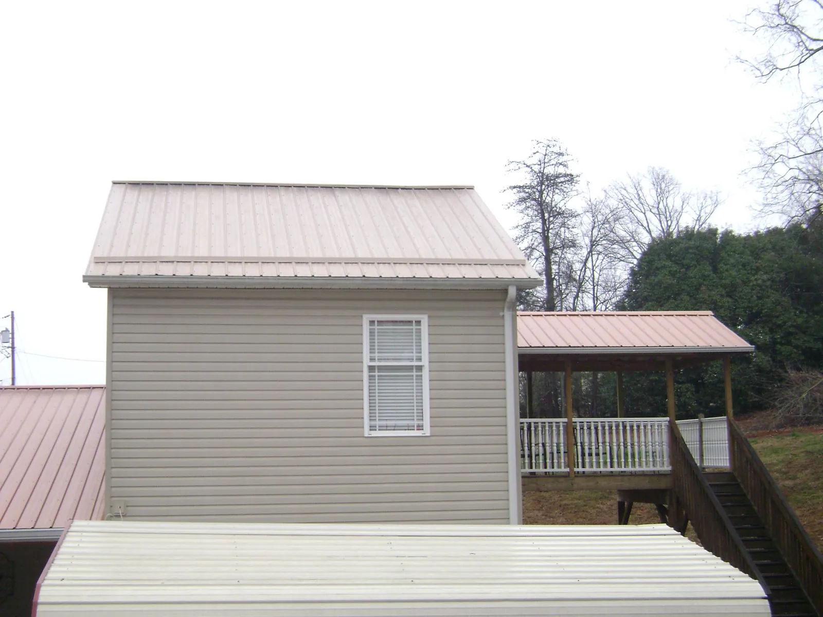 Tan metal roofs on a two story addition and attached porch, from a Roof Replacement job in Vancleave